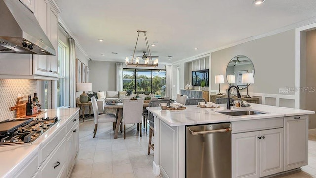 kitchen with under cabinet range hood, a sink, open floor plan, crown molding, and appliances with stainless steel finishes