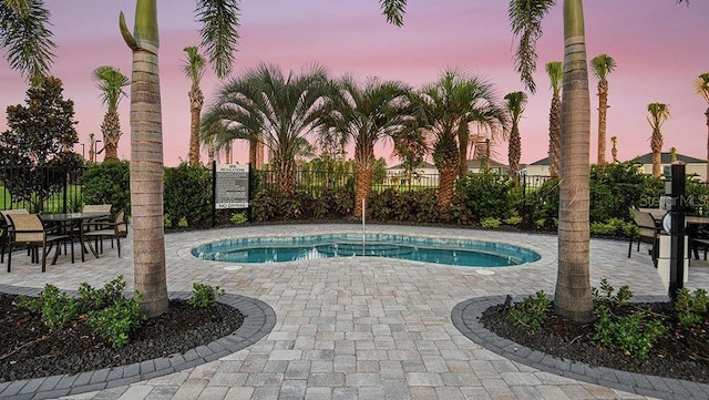pool at dusk with a pool, a patio, and fence