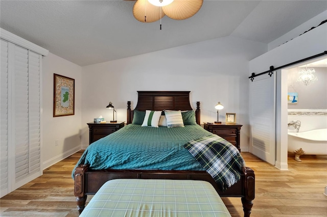 bedroom featuring vaulted ceiling, light wood-style floors, a barn door, baseboards, and a ceiling fan
