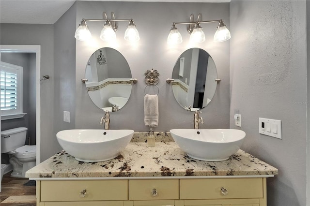 bathroom featuring wood finished floors, double vanity, and toilet