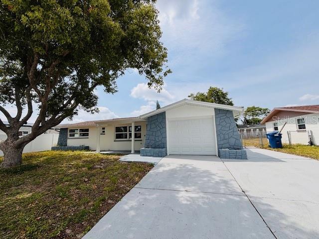 6046 7th Ave, New Port Richey, FL 34653 - single story home with an attached garage, driveway, stone siding, and fence