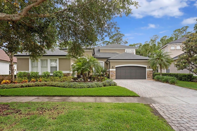 view of front of property with stucco siding, a garage, decorative driveway, stone siding, and a front lawn