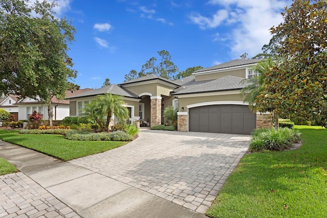 view of front of home featuring stucco siding, an attached garage, decorative driveway, a front lawn, and stone siding