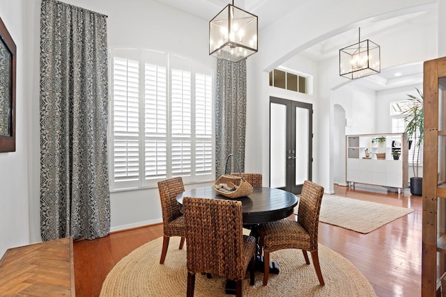 dining room with a chandelier, arched walkways, wood finished floors, french doors, and baseboards