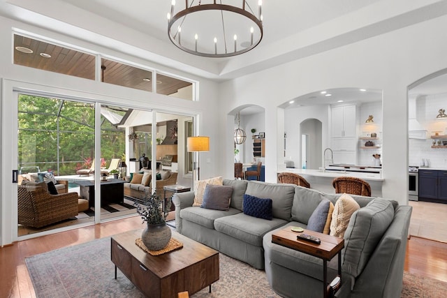 living area with arched walkways, light wood-style floors, a chandelier, and recessed lighting