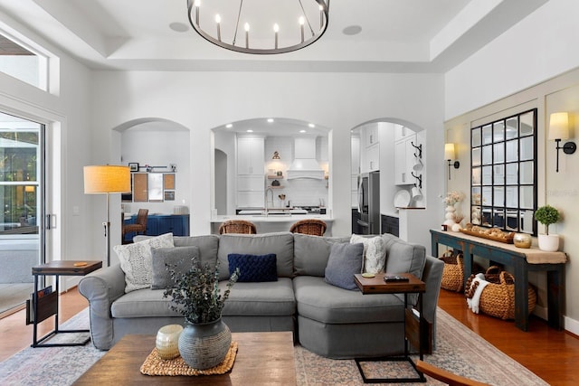 living room with arched walkways, a high ceiling, a chandelier, wood finished floors, and a raised ceiling