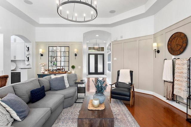 living area with arched walkways, a chandelier, a tray ceiling, and wood finished floors