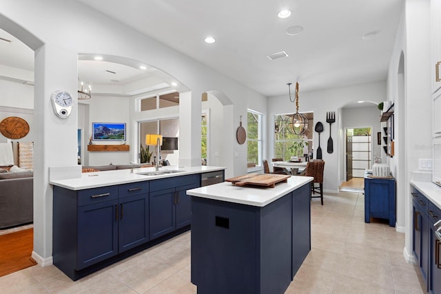 kitchen with a sink, blue cabinetry, arched walkways, light countertops, and a center island