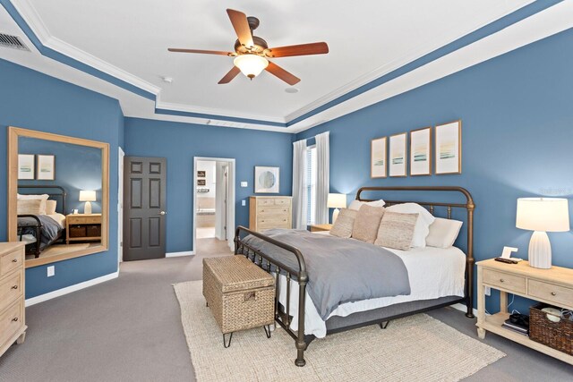carpeted bedroom with a tray ceiling, crown molding, a ceiling fan, baseboards, and ensuite bathroom