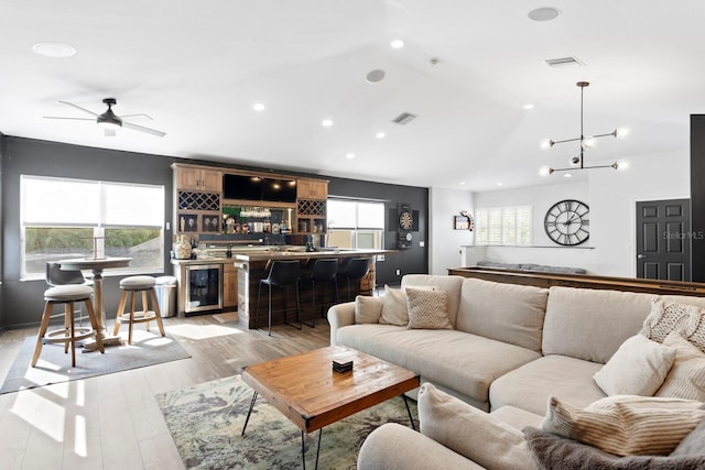 living room with lofted ceiling, bar with sink, beverage cooler, recessed lighting, and light wood-type flooring