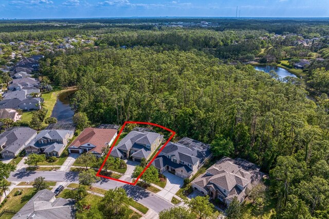 view of property location featuring a forest, property parcel outlined, nearby suburban area, and a large body of water