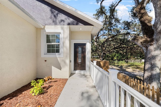 entrance to property featuring fence and stucco siding