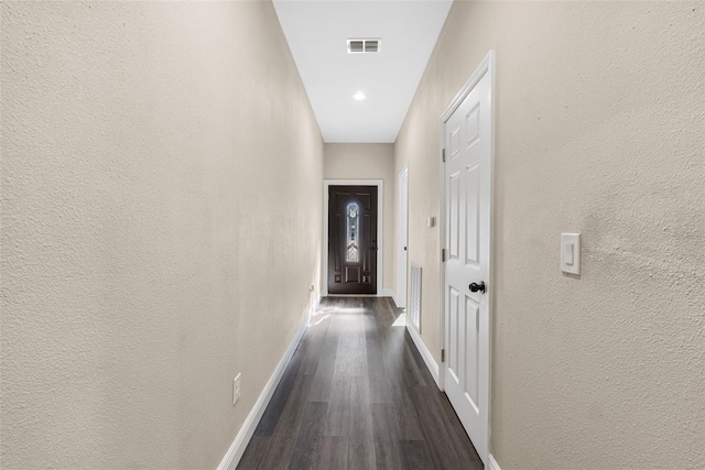 hallway featuring visible vents, dark wood-style flooring, baseboards, and a textured wall