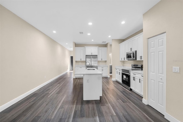 kitchen featuring baseboards, a sink, stainless steel appliances, an island with sink, and dark wood-style floors