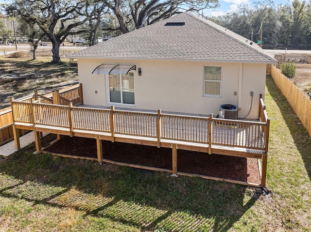 back of property featuring cooling unit, stucco siding, a deck, fence, and a shingled roof