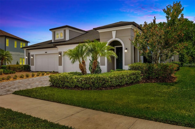 view of front of property with stucco siding, a lawn, decorative driveway, and an attached garage
