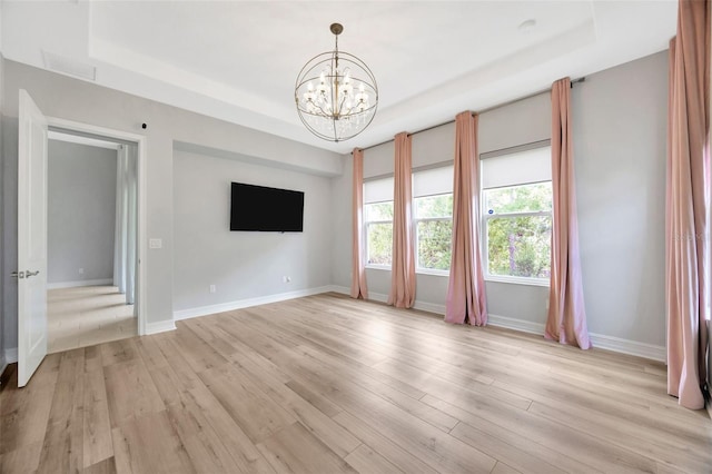 unfurnished living room with a raised ceiling, a chandelier, light wood-style floors, and baseboards