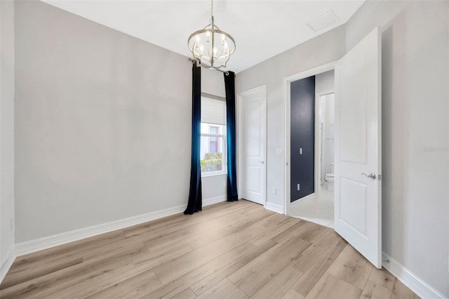spare room with light wood-style flooring, a chandelier, and baseboards