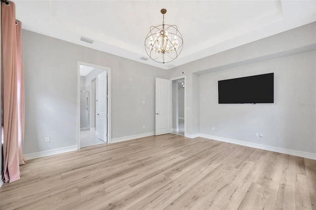 unfurnished bedroom with a tray ceiling, a chandelier, and light wood finished floors