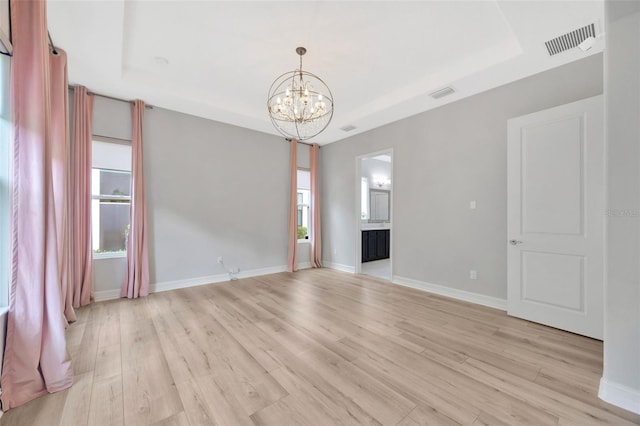 spare room featuring a chandelier, light wood finished floors, a raised ceiling, and baseboards