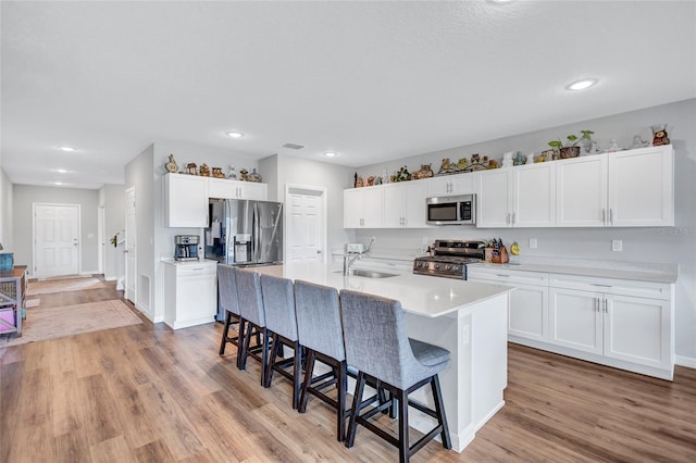 12710 Hysmith Loop, Parrish, FL 34219 - kitchen with appliances with stainless steel finishes, a kitchen breakfast bar, a sink, light wood-style flooring, and white cabinets