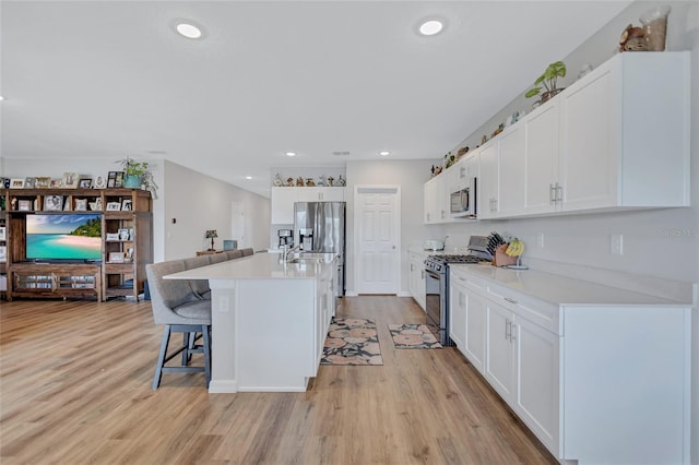 12710 Hysmith Loop, Parrish, FL 34219 - kitchen with stainless steel appliances, light wood-style flooring, light countertops, a kitchen breakfast bar, and white cabinetry