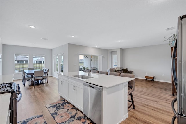 12710 Hysmith Loop, Parrish, FL 34219 - kitchen featuring stainless steel appliances, a sink, white cabinetry, a center island with sink, and light wood-style floors