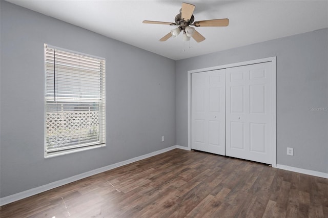 unfurnished bedroom with multiple windows, dark wood-style floors, baseboards, and a closet