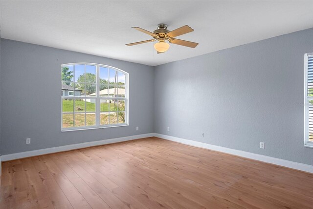 empty room with ceiling fan, light wood-style floors, and baseboards