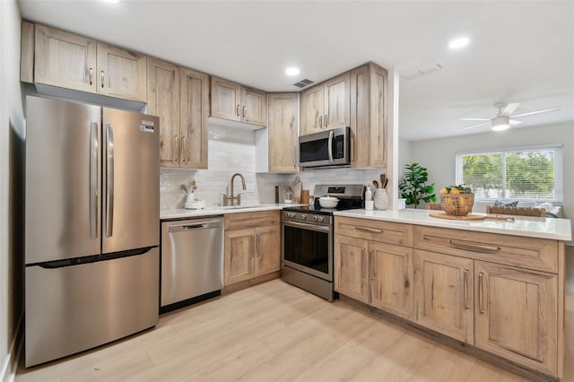 kitchen with stainless steel appliances, tasteful backsplash, a peninsula, light wood-style floors, and light countertops