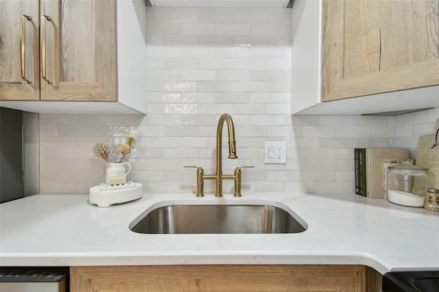 kitchen with a sink, decorative backsplash, light stone countertops, and dishwashing machine