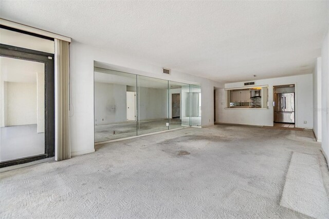 unfurnished living room with carpet flooring, a textured ceiling, and baseboards