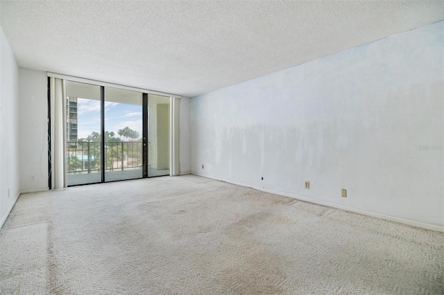 spare room with a wall of windows, carpet flooring, a textured ceiling, and baseboards