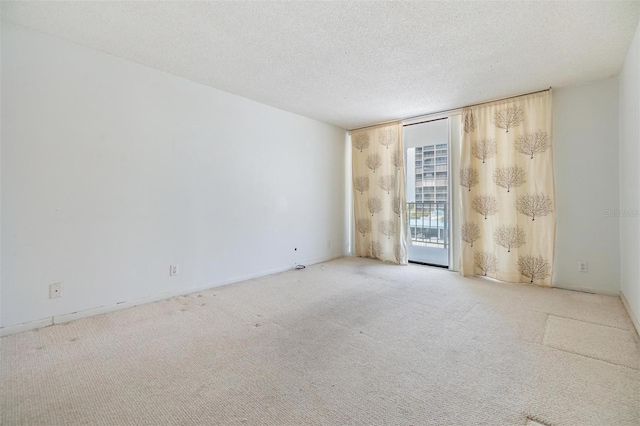 spare room with a wall of windows, carpet floors, a textured ceiling, and baseboards
