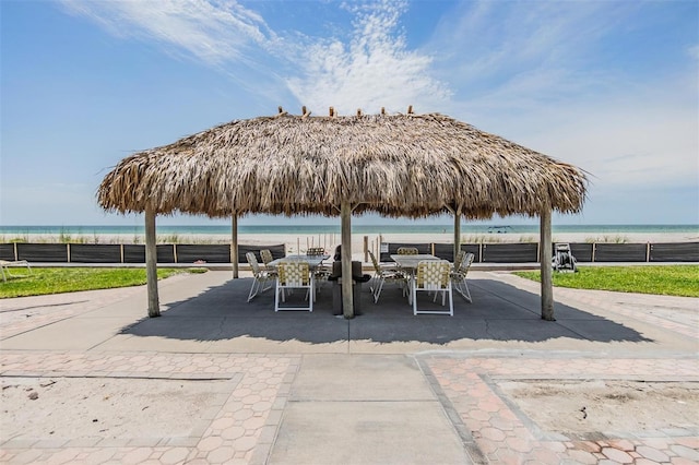 surrounding community featuring view of water and beach, fence, outdoor dining space, and a patio