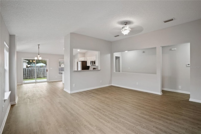 unfurnished living room featuring a textured ceiling, baseboards, visible vents, ceiling fan with notable chandelier, and wood finished floors