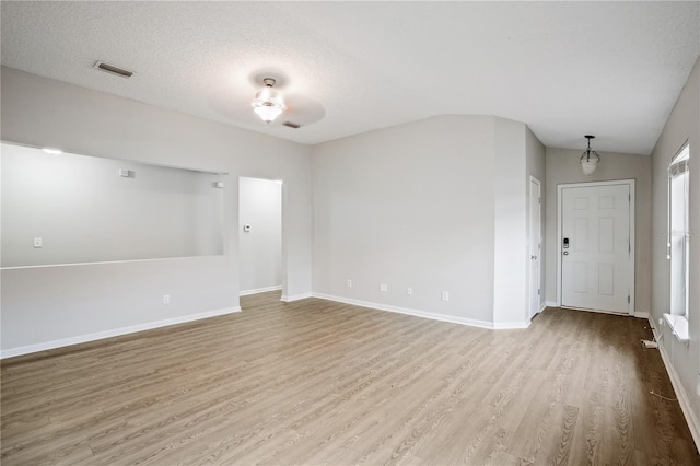 unfurnished room featuring lofted ceiling, a textured ceiling, baseboards, visible vents, and wood finished floors