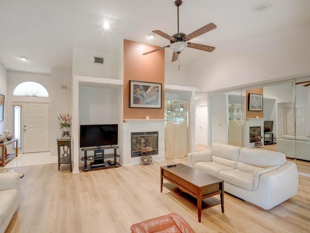 living room featuring a tiled fireplace, ceiling fan, light wood-style flooring, and high vaulted ceiling