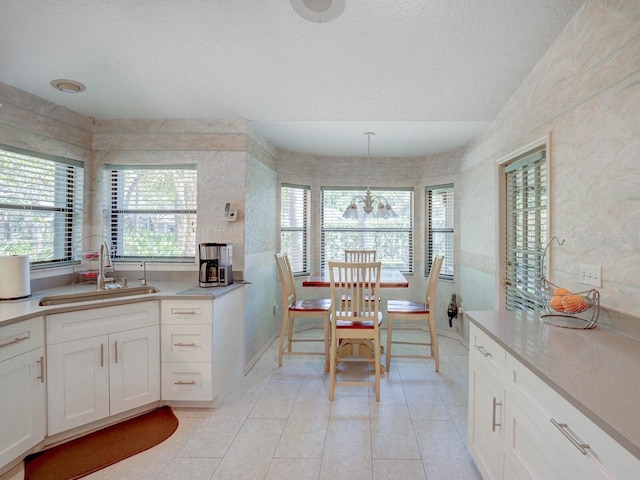 kitchen with a sink, white cabinetry, light countertops, light tile patterned floors, and a textured ceiling