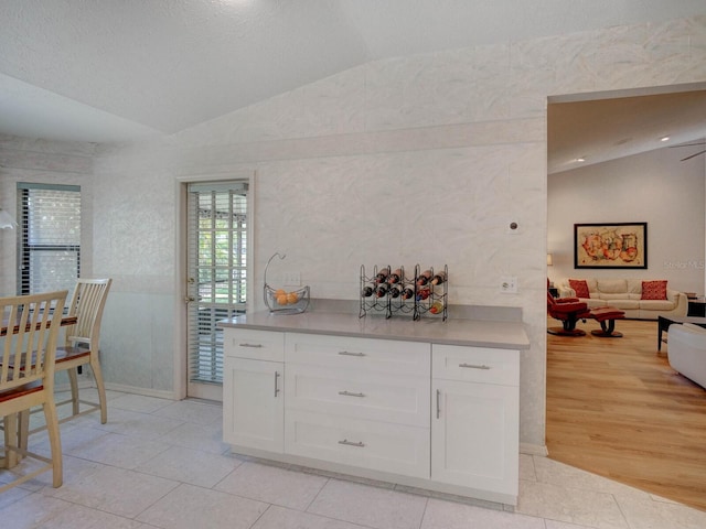kitchen with lofted ceiling, light countertops, white cabinetry, light tile patterned floors, and baseboards