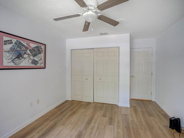 unfurnished bedroom featuring light wood-type flooring, a closet, baseboards, a ceiling fan, and a textured ceiling