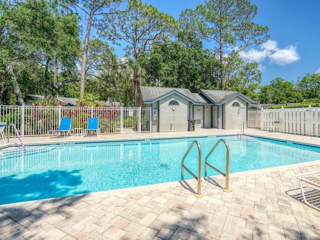 community pool featuring fence, a patio, and view of wooded area