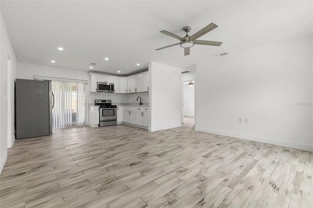 unfurnished living room with ceiling fan, a sink, light wood-style floors, recessed lighting, and baseboards