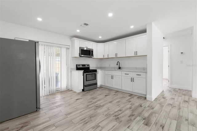 kitchen with appliances with stainless steel finishes, light countertops, light wood-style flooring, white cabinets, and recessed lighting