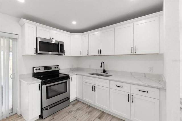 kitchen featuring stainless steel appliances, a sink, white cabinetry, light wood-style flooring, and recessed lighting