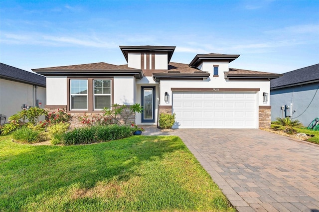 prairie-style home featuring stone siding, stucco siding, a front yard, a garage, and decorative driveway