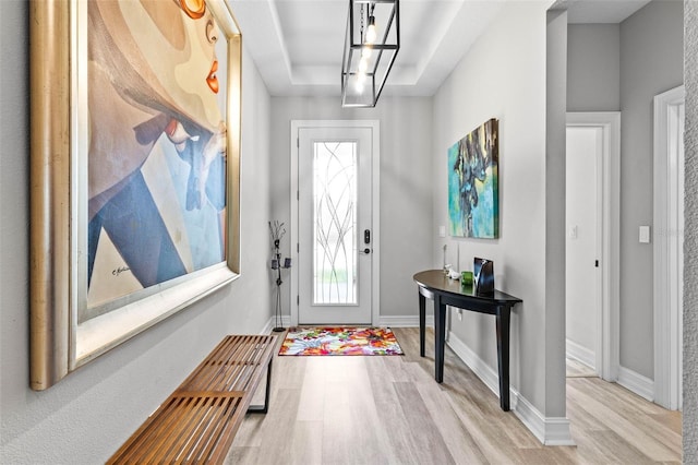entryway with wood finished floors, a tray ceiling, baseboards, and a chandelier