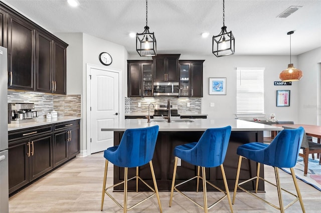 kitchen with appliances with stainless steel finishes, a breakfast bar area, backsplash, decorative light fixtures, and a textured ceiling