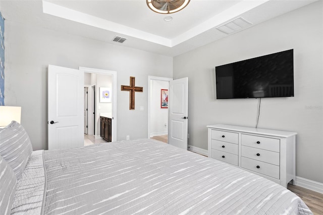 bedroom with light wood-style floors, baseboards, and a tray ceiling