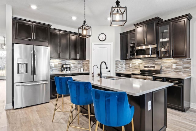kitchen featuring stainless steel appliances, a sink, light countertops, glass insert cabinets, and tasteful backsplash